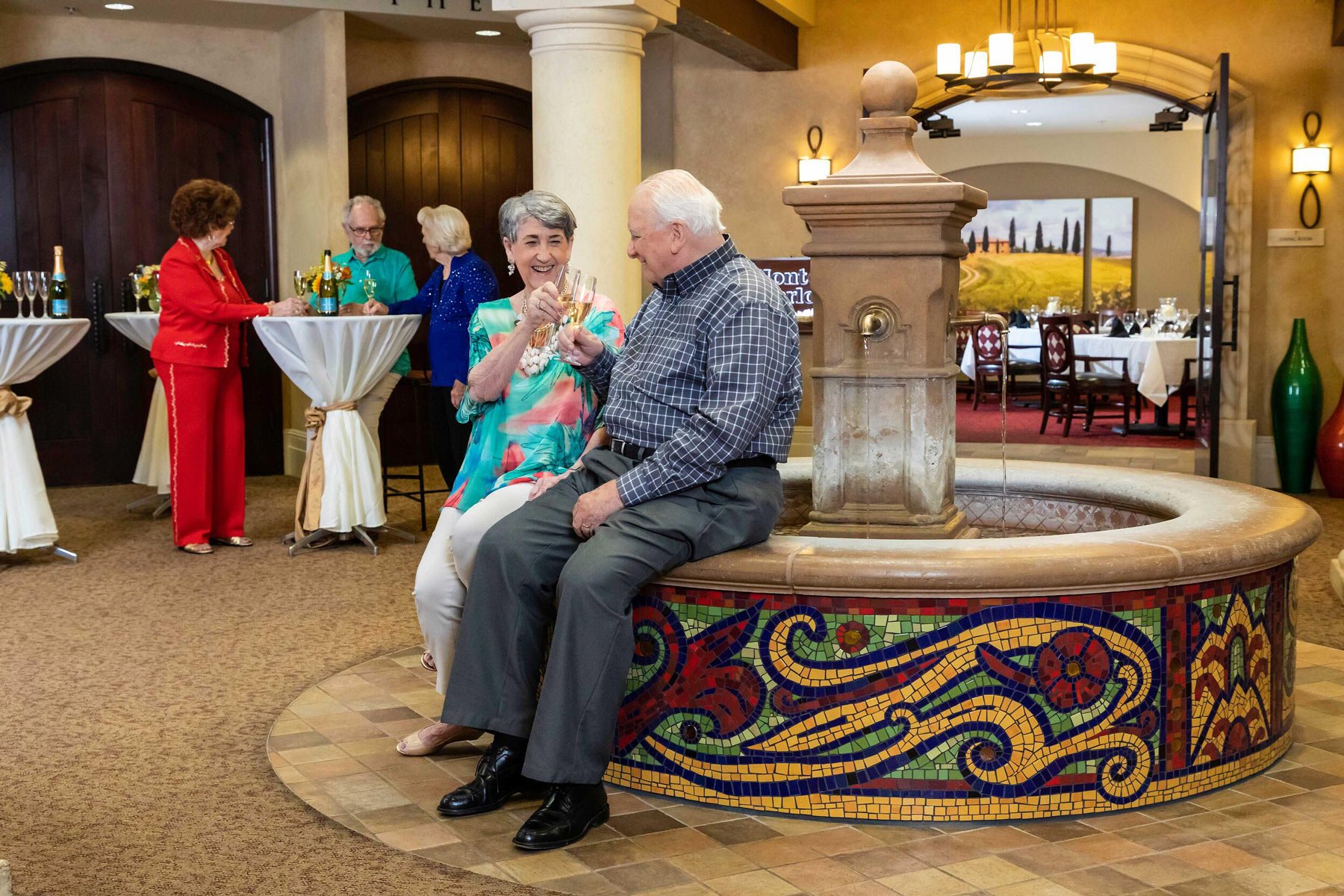 Senior couple sitting on the edge of a fountain toasting with Champagne glasses